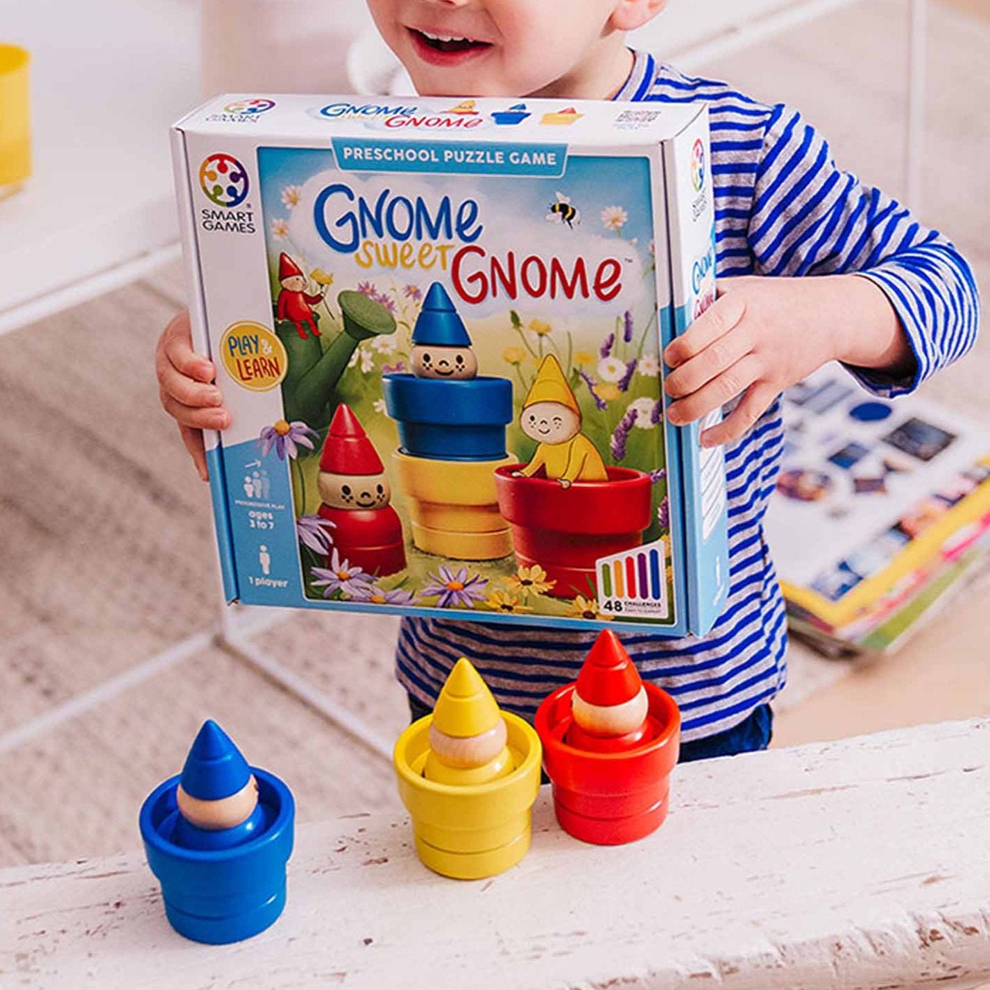 Photo of child holding box of Gnome Sweet Gnome by Smart Games.  The pots and gnomes are lined up on a shelf in front of them.