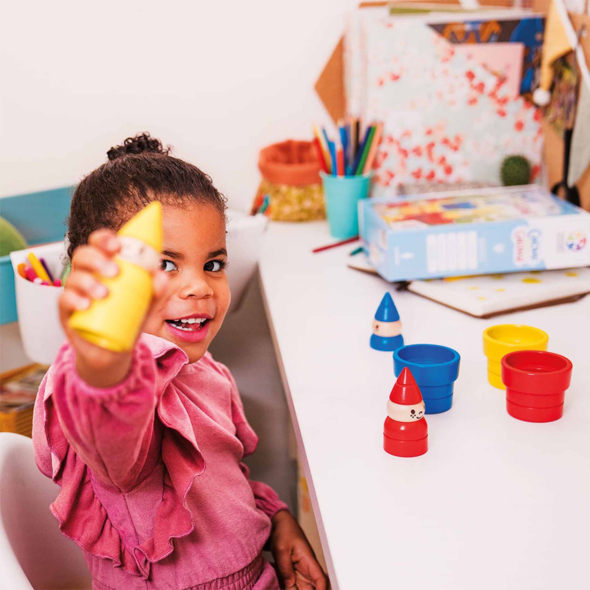 Photo of child sitting at a table holding up the yellow gnome while playing Gnome Sweet Gnome by Smart Games.