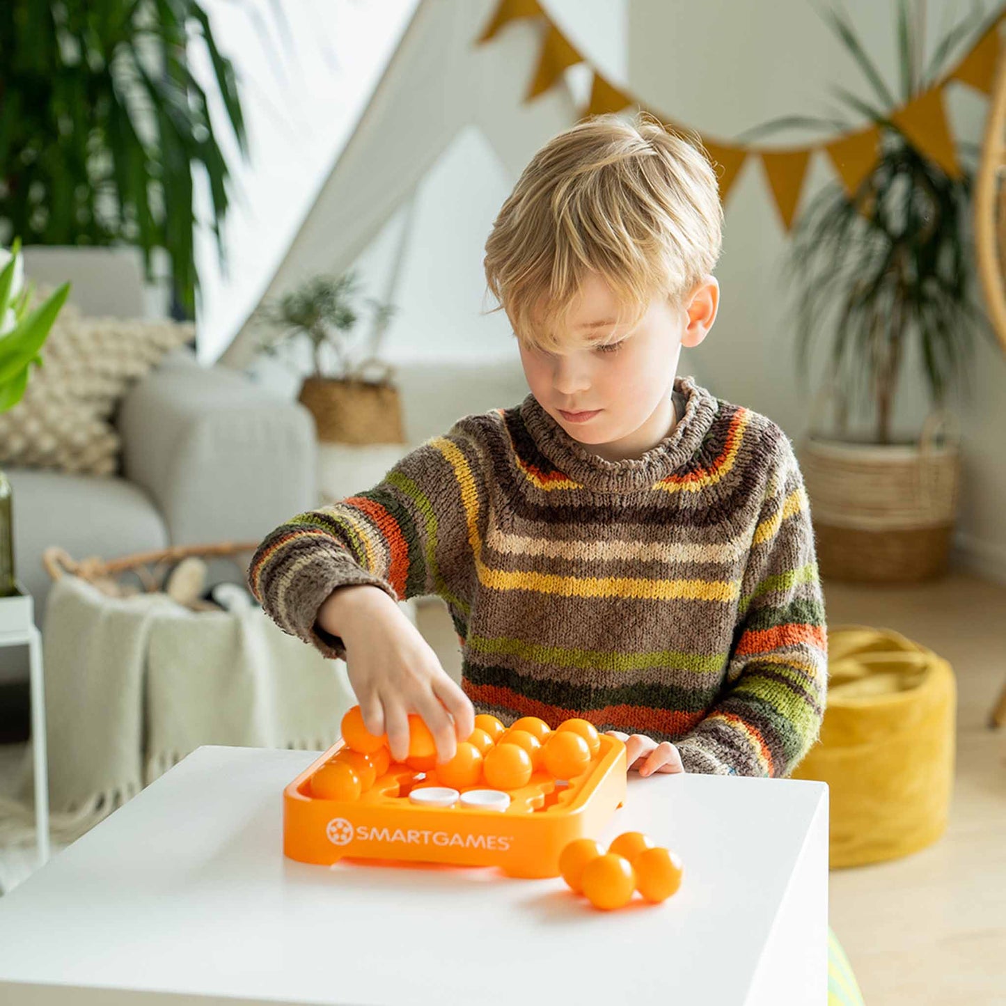 Photo of child in a stripey jumper playing IQ Mini XXL mind puzzle by Smart Games.